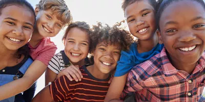 group of kids shoulder to shoulder surrounding the viewer and smiling