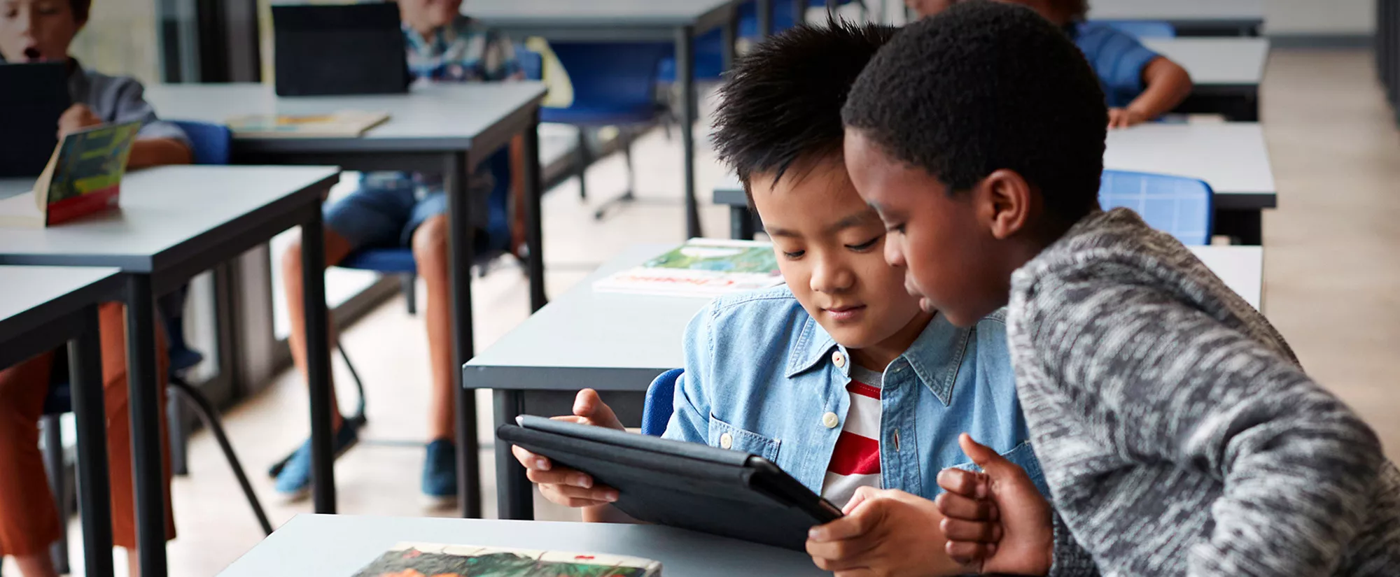 Two boys reading a digital book on a tablet in a classroom