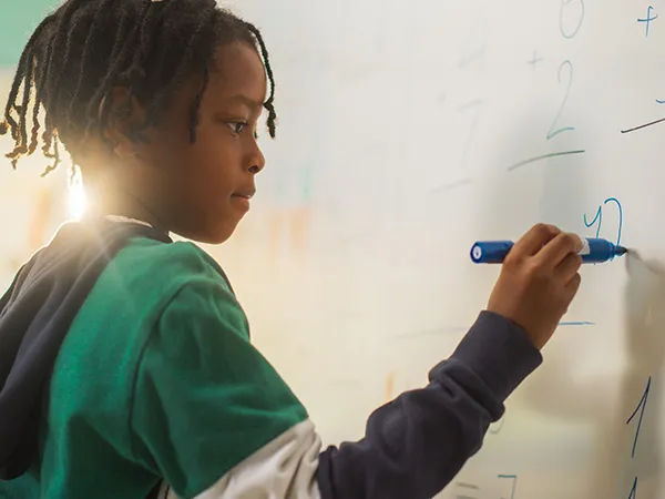 Male student doing a math problem on a whiteboard