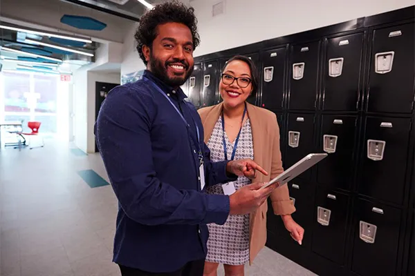 Two school administrators standing in a school hallway, reviewing information in myON on a tablet as one points to the screen